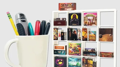 A white ceramic cup filled with pens and a stapler sits on the left. To the right is a white grid-style shelf holding multiple small board game boxes, including visible titles such as "GLOOMHAVEN", "MARS", "POTION EXPLOSION", "DICED VEGGIES", "TERRAFORMING MARS", "CUBITOY", "Sleeping Gods", and others.