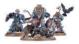 A detailed display features a group of new Space Wolves miniatures, prominently showcasing Logan Grimnar in ornate terminator armor, adorned with a fur cloak and wielding his axe, Morkai. He is flanked by two wolves, Tyrnak and Fenrir, and accompanied by his lieutenants, Arjac Rockfist and Njal Stormcaller, who are also intricately designed. The scene is set on rocky terrain with scattered skulls and grass, enhancing the fierce and wild aesthetic of the Space Wolves.