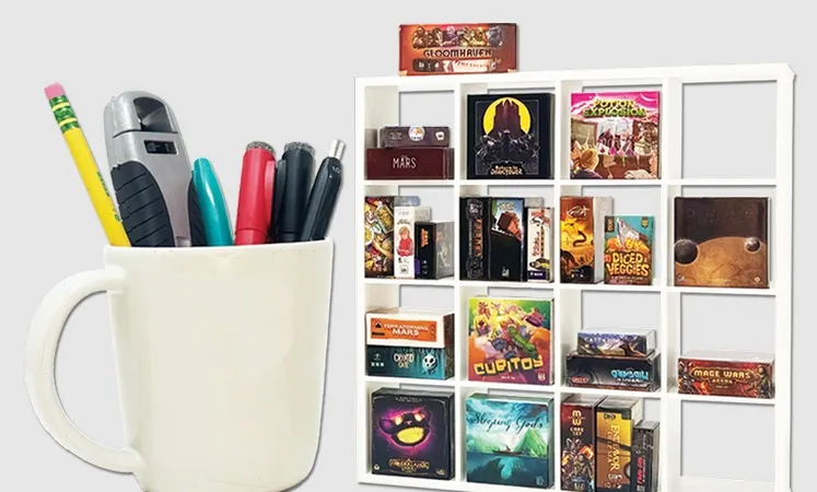 A white ceramic cup filled with pens and a stapler sits on the left. To the right is a white grid-style shelf holding multiple small board game boxes, including visible titles such as "GLOOMHAVEN", "MARS", "POTION EXPLOSION", "DICED VEGGIES", "TERRAFORMING MARS", "CUBITOY", "Sleeping Gods", and others.