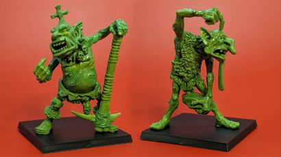 Two green hill troll miniatures are displayed against a bright red background. On the left, Thoughtful Grog stands with a large club raised high, showcasing a stout body and a rugged appearance. On the right, Grobna the Maw is depicted in a dynamic pose, holding a rock and featuring exaggerated facial features, including a long tongue and wild hair, both designed to fit on 40mm bases.