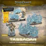 Three metallic miniature figures of Protoss hero Tassadar in blue armor, posed on rocky terrain. Packaging box behind shows "StarCraft Tabletop Miniatures Game," "Protoss," "3 Miniatures," and "Tassadar." Text reads "Tassadar New Protoss Hero" and "Ø 40mm."