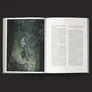 A darkly illustrated page from the "City of My Nightmares" campaign book features a haunting figure suspended in mid-air, with long hair and elongated limbs, surrounded by swirling shadows. The figure appears to be emerging from a dimly lit room, adding to the eerie atmosphere. The opposite page contains text detailing aspects of the campaign, with a focus on the narrative and character elements.