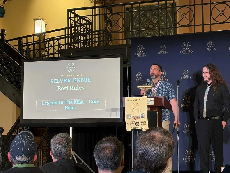 Man at podium with trophy, screen reads "SILVER ENNIE Best Rules Legend In The Mist – Core Book"