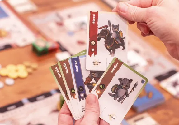 Hand holding illustrated cards: Steed, Urchin, Bandit, Smithy, Soldier.