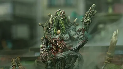 Green-skinned monster with long hair, horns, and a staff, holding a severed head.