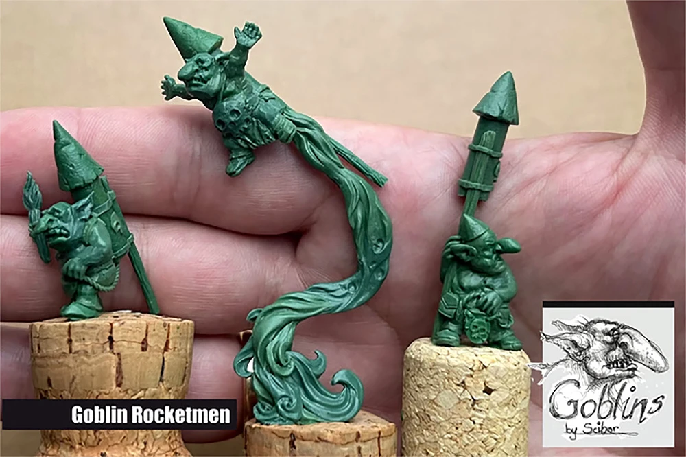 Three green goblin miniatures are displayed, showcasing their whimsical and mischievous designs. The leftmost figure features a goblin wearing a pointed hat, standing on a cork base, while the middle figure depicts a goblin in mid-air, with a flowing tail resembling smoke or energy, holding a skull. The rightmost figure shows another goblin, also on a cork base, holding a spear and wearing a similar pointed hat, emphasizing the playful character of this collection.