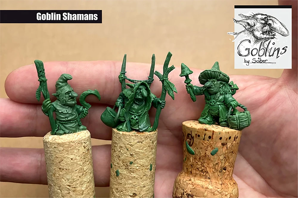 Three green goblin shaman miniatures are displayed on top of cork bases, showcasing their intricate details. The goblins feature various accessories, including staffs and bags, with distinct facial expressions that convey mischief. The background is a neutral color, allowing the vibrant green of the miniatures to stand out prominently.