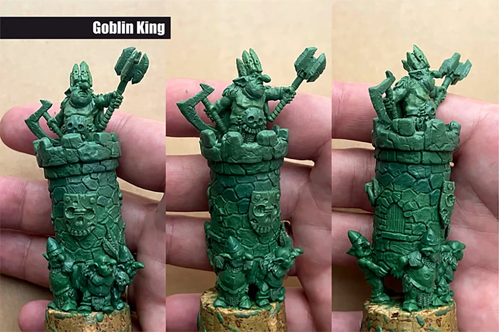 A detailed miniature of a Goblin King stands atop a stone tower, holding a large axe and raising a fist in triumph. The tower features a textured stone design with a skull motif and a shield emblem, while smaller goblins are depicted at the base, adding to the scene's character. The miniature is presented in a green resin finish, showcasing intricate details and dynamic poses.