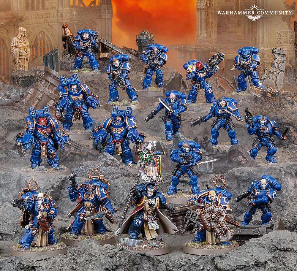 A group of Ultramarine Space Marines is displayed prominently against a rocky, war-torn backdrop. The figures are painted in vibrant blue armor, featuring various poses and weaponry, including bolters and a power sword. In the center, Chief Librarian Tigurius stands out in a flowing robe, holding a staff and flanked by several other Ultramarines, showcasing a mix of infantry types, including Bladeguard Veterans and Aggressors.