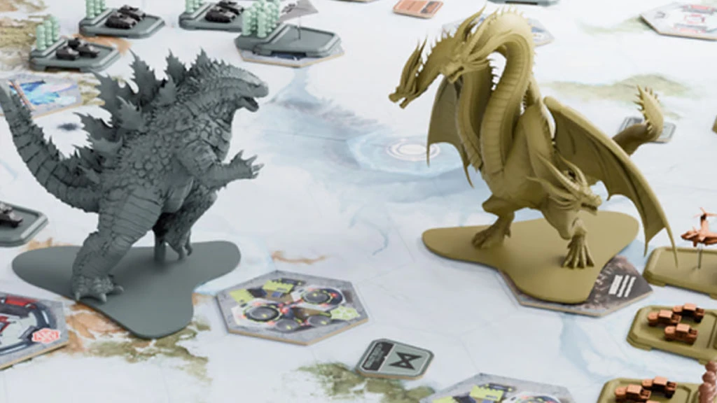 A detailed tabletop scene features two large miniatures: Godzilla in a gray color and King Ghidorah in a tan color, positioned on a game board with various hexagonal tiles. Surrounding them are additional game elements, including armored vehicles and other tokens, set against a backdrop that suggests a dynamic battlefield. The overall composition highlights the cinematic combat theme of the game, emphasizing the iconic nature of the monsters.