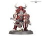 A muscular warrior stands prominently, adorned in red and black armor with sharp spikes and skull motifs. He wields a large, menacing axe in one hand and a shield with jagged edges in the other, both showcasing intricate detailing. His head is covered by a horned helmet, and he stands on a rocky base with sparse grass and skulls scattered around.