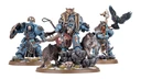A detailed display features a group of new Space Wolves miniatures, prominently showcasing Logan Grimnar in ornate terminator armor, adorned with a fur cloak and wielding his axe, Morkai. He is flanked by two wolves, Tyrnak and Fenrir, and accompanied by his lieutenants, Arjac Rockfist and Njal Stormcaller, who are also intricately designed. The scene is set on rocky terrain with scattered skulls and grass, enhancing the fierce and wild aesthetic of the Space Wolves.