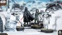 A detailed scene features Darth Vader standing prominently with his red lightsaber drawn, dressed in his iconic black armor and cape. Flanking him are two Stormtroopers, one aiming a blaster, set against a snowy landscape with scattered debris and structures. The miniatures are mounted on circular bases, showcasing their intricate designs and the dynamic pose of the characters.