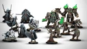A collection of highly detailed miniatures from the new Warmachine starter set, "Frozen and Forgotten," features two distinct warbands. On the left, dark elves Nyss hunters are represented, including Lanyssa Ryssyl, a character in ornate armor, and various character warbeasts, all in dark and muted colors. On the right, the ogres Orgoth Graveborn are led by Anathia, the Imperishable Desolation, clad in heavy armor with green accents, alongside other character units, showcasing a mix of dark and metallic tones. The miniatures are set against a light background, highlighting their intricate designs.