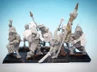 A collection of 28mm scale skeleton warriors from Diehard Miniatures, featuring several figures in various poses. The miniatures are equipped with weapons such as spears and swords, and are adorned with armor and helmets reminiscent of classic Oldhammer designs. The background is a soft blue gradient, highlighting the details of the skeletal figures, which are mounted on black bases.