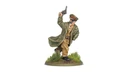 A miniature figure of Lieutenant-General Sir Adrian Carton de Wiart VC is depicted in a dynamic pose, raising a revolver in one hand while wearing a military uniform complete with a long coat and a peaked cap adorned with insignia. The figure stands on a circular base featuring tufts of grass and earthy terrain, emphasizing a battlefield setting. The detailed paintwork highlights his facial features, including a mustache and sunglasses, capturing a spirited and commanding presence.