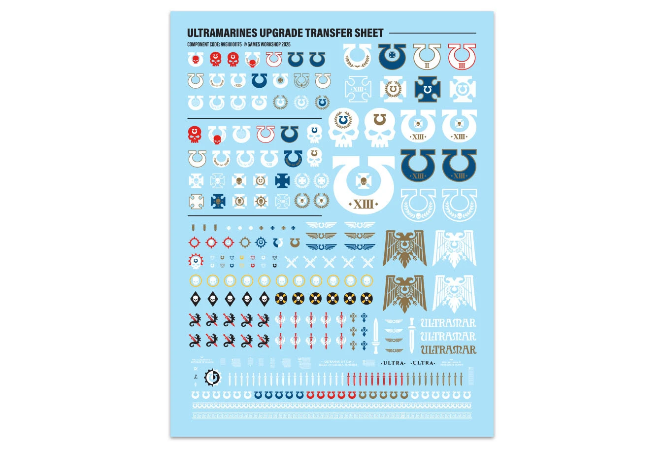 A transfer sheet featuring a variety of Ultramarines decals, set against a light blue background. The sheet includes campaign badges, veterancy markings, and multiple variants of the Ultramarines Chapter icon, along with symbols like skulls, wings, and laurels. Decorative borders and trim decals are also present, providing options for customizing models with additional flair.