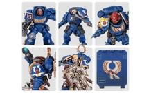 A collection of Ultramarine miniatures showcases various Space Marine figures in blue armor, each featuring distinct details and accessories. The top row includes a character with a prominent helmet and ornate chest emblem, alongside two other figures with different poses and weaponry. The bottom row features a close-up of a figure holding a weapon, another with a skull motif on the armor, and a character wielding a large, intricately designed shield. Additionally, a transfer sheet with various decals is visible, featuring Ultramarine symbols and decorative borders.