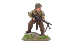 A 28mm scale miniature of a soldier, representing the war hero Audie Murphy, stands on a rocky base adorned with green grass. The figure is dressed in a light green military uniform with insignia on the sleeves and wears a helmet. He holds a machine gun in a ready position, showcasing a determined expression.