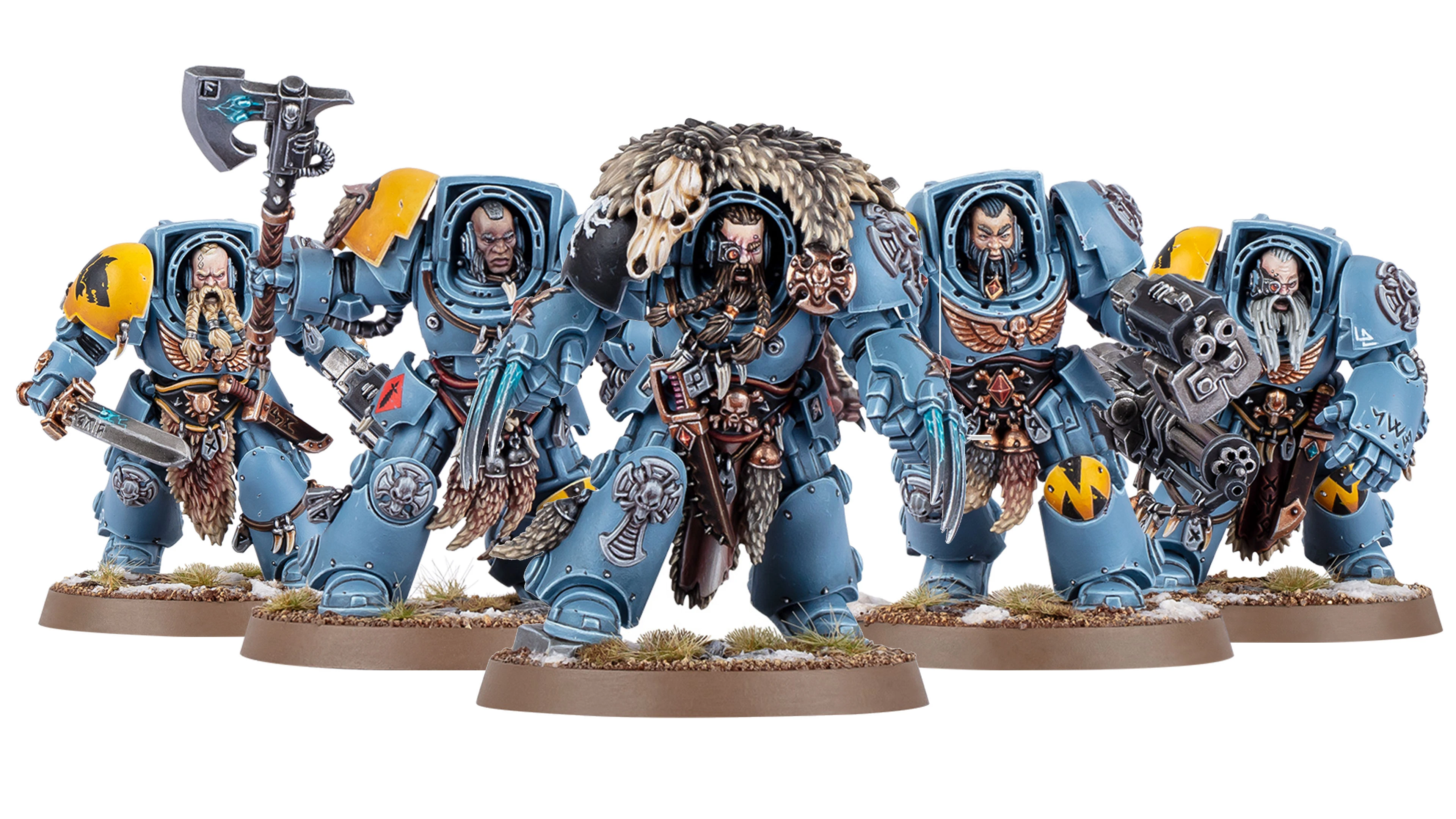 A trio of Space Wolves miniatures stands prominently, showcasing their detailed armor and weaponry. The central figure, likely Logan Grimnar, is adorned in blue terminator armor with a fur cloak and a skull, wielding an axe. Flanking him are two lieutenants: one with a large weapon and intricate details, and the other featuring a distinctive beard and additional armor embellishments, all set against a base with tufts of grass and snow.