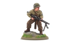 A 28mm scale miniature of a soldier, representing the war hero Audie Murphy, stands on a rocky base adorned with green grass. The figure is dressed in a light green military uniform with insignia on the sleeves and wears a helmet. He holds a machine gun in a ready position, showcasing a determined expression.