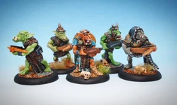 A group of four intricately painted orc miniatures stands against a light blue background. Each orc is armed with various hand weapons, showcasing a mix of colors and details in their armor and features. The miniatures are positioned on round bases adorned with small tufts of grass and skulls, highlighting their dynamic poses and unique characteristics.