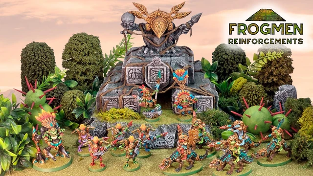 A vibrant scene showcases a variety of colorful Space Frogmen miniatures, including a frogman chieftain and cavalry, positioned around a rocky outcrop adorned with ancient symbols and a large decorative skull. Lush greenery and spiky plants surround the figures, enhancing the fantastical atmosphere. The text "FROGMEN REINFORCEMENTS" is prominently displayed in the corner, indicating the theme of the Kickstarter campaign.