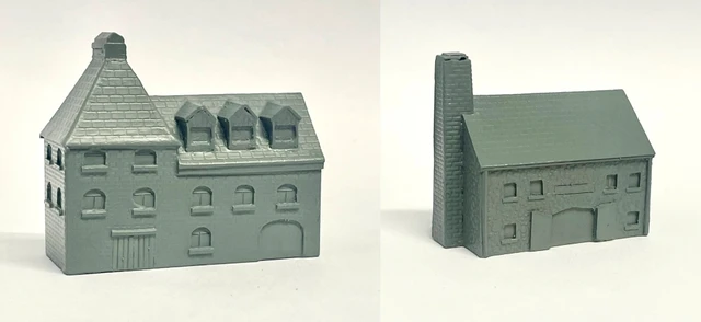 A detailed model of a building designed for 6mm scale wargames, featuring a sloped roof with three dormer windows and a textured surface that resembles slate. The facade includes several arched and rectangular windows, along with a large door at the base, all rendered in a light gray resin. The overall design suggests an industrial style, suitable for various historical or modern warfare settings.