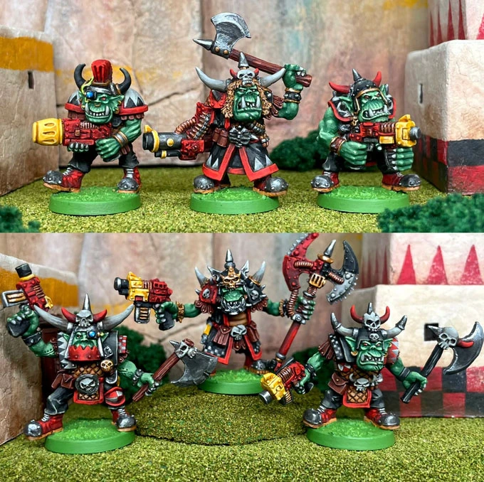 A group of five 28mm scale space orc miniatures is displayed, showcasing their vibrant colors and detailed designs. The top row features orcs in various poses, armed with weapons like a large axe and a futuristic gun, adorned with red and black armor and horned helmets. The bottom row presents another set of orcs, also equipped with axes and guns, emphasizing their fierce appearance with skull motifs and cybernetic enhancements. The backdrop includes a textured surface resembling a rocky terrain, enhancing the overall scene.