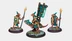 A trio of miniatures from Twilight Miniatures showcases unique characters from the world of Anyaral. On the left, a small humanoid figure holds a spear and wears a shield adorned with turquoise and gold accents. In the center, another figure rides a reptilian creature, also decorated in turquoise, with a large banner attached to its back. The bases of the miniatures feature rocky terrain with patches of green grass, enhancing the fantasy setting.