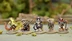 A group of four anthropomorphic miniatures from the game Burrows and Badgers, each character displaying unique features and attire. On the left, a badger holds a rifle, dressed in a green and brown outfit. Next to it, a cat in a blue and red tartan outfit wields a sword. An owl stands in the center, holding a potion, while a rabbit on the right wears a red cloak and holds a dagger. The miniatures are set against a blurred natural background, enhancing their detailed sculpting and painting.