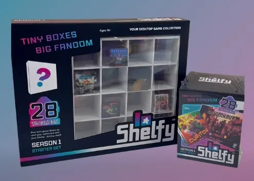 A black Shelfy display case with a clear plastic front, containing 12 small compartments. Some compartments hold miniature board game boxes with visible titles such as "Cascadia" and "Gloomhaven". The display case has text on the left side reading "TINY BOXES BIG FANDOM", "28 TO COLLECT!", "SEASON 1 STARTER SET", and "Ages 14+ YOUR DESKTOP GAME COLLECTION". The Shelfy logo is at the bottom right of the display case. To the right of the display case is a smaller Shelfy box with similar branding and a visible game image on its front. The background is a gradient of purple and blue.