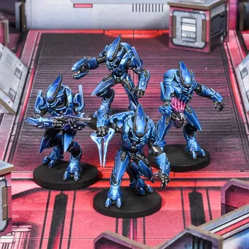 Four Sangheili warriors are depicted in striking blue armor, each wielding different weapons including a needler, plasma rifle, pulse carbine, and energy sword. They are positioned on a futuristic, metallic battlefield with a red and gray color scheme, featuring geometric structures in the background. The warriors exhibit dynamic poses, showcasing their formidable presence as mercenaries in the Halo Flashpoint universe.