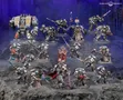 A detailed display of Black Templar miniatures showcases a variety of armored figures in silver and black, set against a dark, rocky backdrop. Prominent in the scene is a Venerable Dreadnought on the left, flanked by a mix of characters including the Emperor’s Champion, Bladeguard Veterans, and Sword Brethren, all wielding swords and other weapons. The figures are intricately painted, with some holding banners and others poised for battle, creating a dynamic and imposing presence.