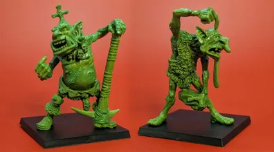 Two green hill troll miniatures are displayed against a bright red background. On the left, Thoughtful Grog stands with a large club raised high, showcasing a stout body and a rugged appearance. On the right, Grobna the Maw is depicted in a dynamic pose, holding a rock and featuring exaggerated facial features, including a long tongue and wild hair, both designed to fit on 40mm bases.