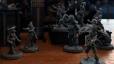 A collection of detailed miniatures from the game "Boarders and Black Flags" features a mix of human pirates and undead skeletons. The pirates are depicted in dynamic poses, some wielding swords and others holding various pirate-themed accessories, showcasing their character and personality. In the background, a wooden structure resembling a ship's deck adds context to the scene, enhancing the overall pirate theme.