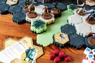 A tabletop scene features several miniatures from the G.I. JOE Heroscape game positioned on modular hex terrain. The terrain includes a mix of dark hexes and light green tiles, with some areas showcasing foliage. In the foreground, a "Jump Pack" card and red wound markers are visible, alongside dice, enhancing the gameplay setup.