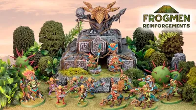 A vibrant scene showcases a variety of colorful Space Frogmen miniatures, including a frogman chieftain and cavalry, positioned around a rocky outcrop adorned with ancient symbols and a large decorative skull. Lush greenery and spiky plants surround the figures, enhancing the fantastical atmosphere. The text "FROGMEN REINFORCEMENTS" is prominently displayed in the corner, indicating the theme of the Kickstarter campaign.