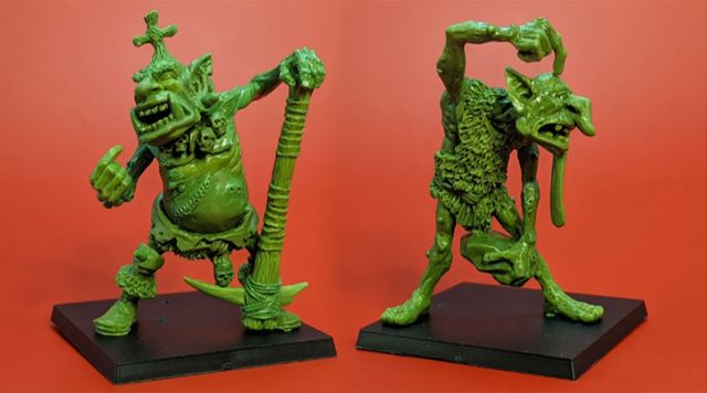 Two green hill troll miniatures are displayed against a bright red background. On the left, Thoughtful Grog stands with a large club raised high, showcasing a stout body and a rugged appearance. On the right, Grobna the Maw is depicted in a dynamic pose, holding a rock and featuring exaggerated facial features, including a long tongue and wild hair, both designed to fit on 40mm bases.