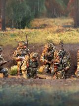 A group of six British army miniatures is depicted in a natural setting, with a backdrop of greenery and a hint of rain. The soldiers are dressed in modern camouflage uniforms and equipped with various weapons, including rifles and gear typical of contemporary military operations. They are positioned in a tactical formation, some seated and others standing, showcasing a range of unique sculpts that highlight their individual poses and details.