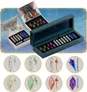 Open black box with 12 colorful gem-like objects inside, each shaped like a sword hilt with a glowing core. Two open display cases show similar items in trays. Artwork depicts fantasy characters and a map. Text reads "KININ NUMBERS" and "LIQUID CORE."