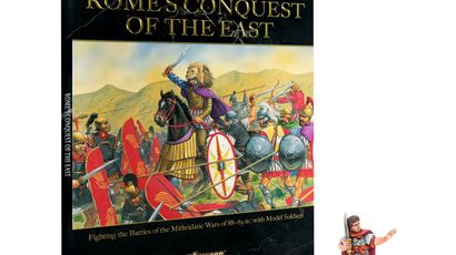 A book titled "Rome's Conquest of the East" from the Hail Caesar series is prominently displayed, featuring a colorful illustration of ancient warriors in battle, including a mounted figure in a purple cloak. The book cover includes the subtitle "Fighting the Battles of the Mithridatic Wars of 88-63 BC with Model Soldiers." Next to the book, there is a miniature figure of Julius Caesar, depicted in early Roman armor, holding a sword and standing on a small base with grass.