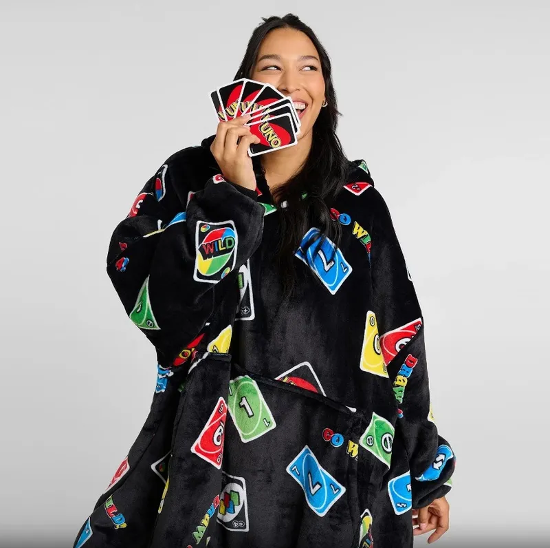 Woman in UNO card-patterned black hooded blanket holding UNO cards.