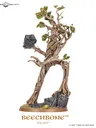 A towering model of Beechbone, an ent from the Middle-earth Strategy Battle game, stands prominently with a rugged, bark-like texture and intricate details. His limbs are gnarled and branch-like, adorned with vibrant green leaves, while he holds a large rock in one hand. The base features rocky terrain with patches of grass, emphasizing his formidable presence on the battlefield.