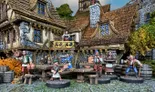 A detailed scene depicts a bustling tavern setting with several 28mm scale white metal miniatures representing various townsfolk. Characters include a barmaid serving drinks, a bard playing music, and patrons engaged in conversation, all set against a backdrop of a rustic tavern with a thatched roof and stone walls. The environment features wooden tables, barrels, and vibrant foliage, creating a lively atmosphere typical of a fantasy RPG setting.