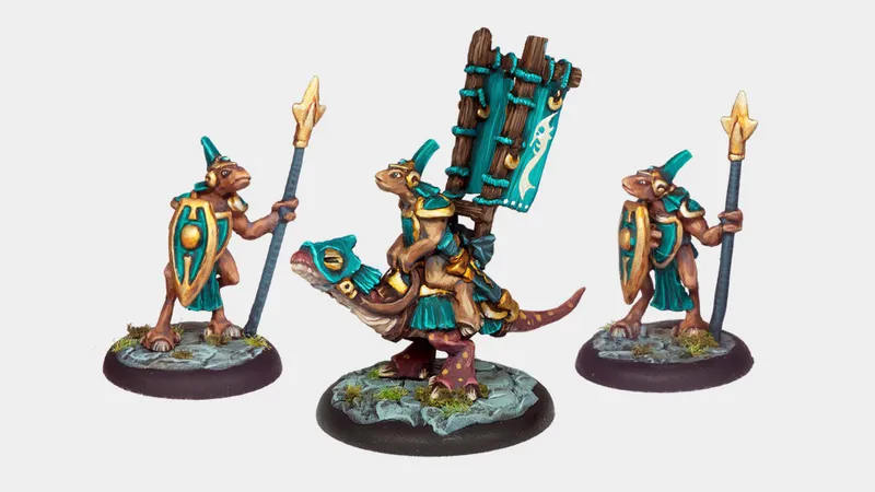 A trio of miniatures from Twilight Miniatures showcases unique characters from the world of Anyaral. On the left, a small humanoid figure holds a spear and wears a shield adorned with turquoise and gold accents. In the center, another figure rides a reptilian creature, also decorated in turquoise, with a large banner attached to its back. The bases of the miniatures feature rocky terrain with patches of green grass, enhancing the fantasy setting.