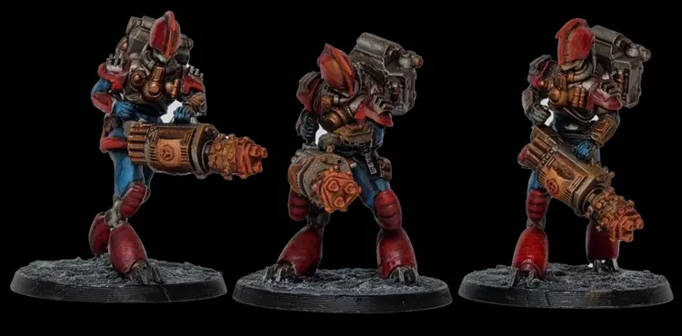 Three intricately designed miniatures stand against a black background, showcasing a futuristic aesthetic. Each figure features a robust build with prominent red and blue armor, detailed mechanical components, and unique weaponry, including a large, cylindrical device and a smaller, handheld weapon. The bases are textured to resemble rocky terrain, enhancing the overall sci-fi theme of the miniatures.