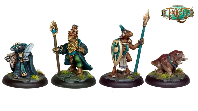 A trio of miniatures from Twilight Miniatures showcases characters from the world of Anyaral. In the center, a humanoid figure with a shield and spear wears a tunic and has a distinctive headdress, flanked by two smaller creatures: one resembling a small dinosaur with a collar, and another figure in a dark outfit on the left. The bases of the miniatures are adorned with tufts of grass, enhancing their fantasy aesthetic. The Twilight logo is displayed in the top corner.