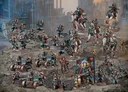 A detailed display of the Death Korps of Krieg models features a variety of miniatures, including ten troopers, a Command Squad, a Heavy Weapons Squad, and five cavalry riders on horses. The models are painted in muted tones of blue and gray, with some adorned in red accents, set against a rocky terrain backdrop. A flag bearing the Death Korps insignia and a few heavy weapon emplacements are also visible, emphasizing their military theme.