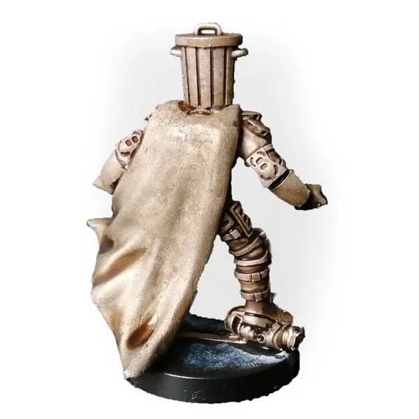 A 28mm scale miniature figure of a humanoid character wearing a brown, tattered cape and a bucket-like headpiece resembling a trash bin. The figure has a mechanical or armored appearance with segmented joints and details on the limbs. It stands on a round black base.